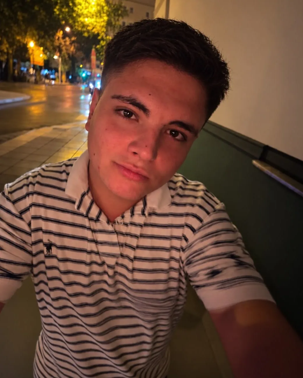 Retrato de Aaron Alba de noche, con un polo de rayas, en una calle iluminada