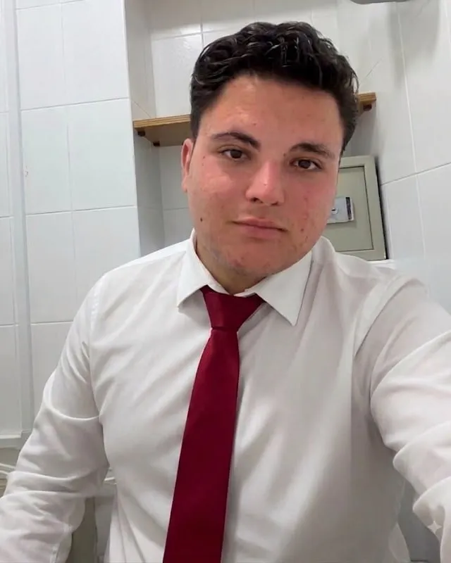 Aaron Alba con camisa blanca y corbata roja, serio, mirando a cámara